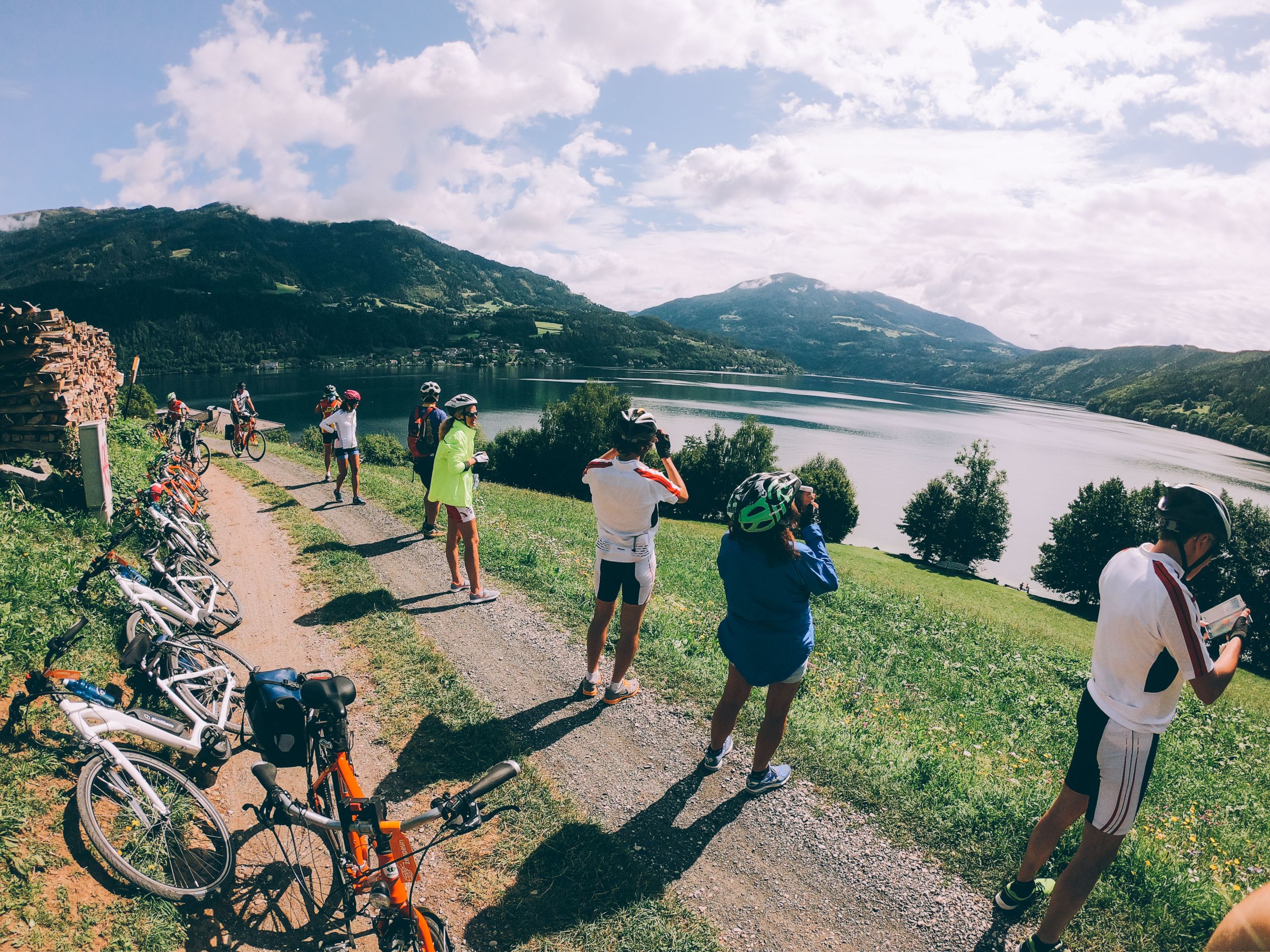 Gruppo di ciclisti che percorre un sentiero verde lungo la Ciclovia dell'Alpe Adria con vista sulle montagne, Austria.